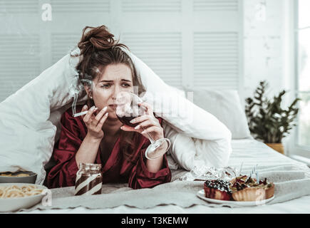 Deprimiert Frau Rauchen im Bett und Wein zu trinken Stockfoto