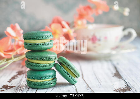 Stapel von frischem französischen Grünen Tee macarons auf einem weißen rustikalen Tisch mit Blumen und antiken Tasse Tee unscharf im Hintergrund.. Stockfoto