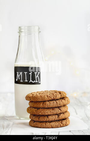 Stapel von frischen, hausgemachten Haferflocken Cookies mit einer Flasche Milch auf einem weißen Tisch vor einem weißen Hintergrund. Stockfoto