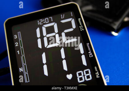 Nahaufnahme von isolierten digitalen Monitor Manometer mit Manschette mit hohen diastolischen und systolischen Blutdruck. Blauen Hintergrund. Stockfoto