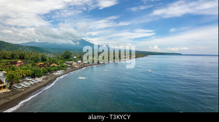 Panoramablick auf das Luftbild von Amed Beach in Bali, Indonesien. Traditionelle Fischerboote namens jukung am schwarzen Sandstrand und Mount Agung Vulkan in der Stockfoto