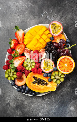 Leckere Obstplatte mango Papaya orangen Leidenschaft Früchte Beeren auf ovalen Servierteller auf dunklen konkreten Hintergrund, Ansicht von oben, selektiver Fokus, Stockfoto