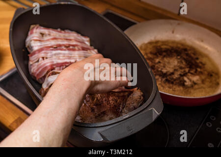 Die Hand einer Frau füllt einen Braten mit Speck Stockfoto