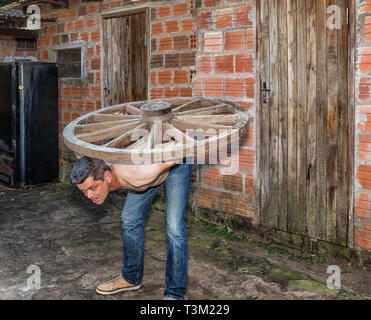 Ein Mann trägt ein hölzernes Rad auf seinem Rücken. Stockfoto