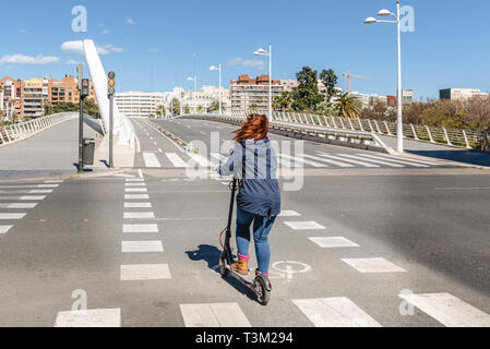 Frau auf elektroroller Überqueren einer Straße ohne Autos auf dem Radweg in der Stadt Valencia. Stockfoto