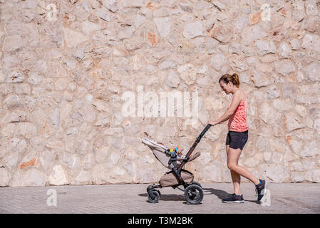 Junge Mutter mit dem Kinderwagen für Ihr Baby nach der Geburt in Form zu bleiben. Stockfoto