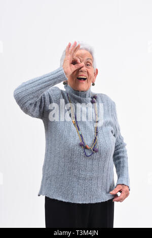 Ältere Frau durch die Finger schauen, als ob Brille trägt auf weißem Hintergrund Stockfoto