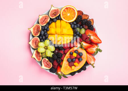 Leckere Obstplatte mango papaya Feigen orangen Beeren auf runder Servierteller auf rosa Hintergrund, Ansicht von oben, selektiver Fokus, kopieren Raum Stockfoto