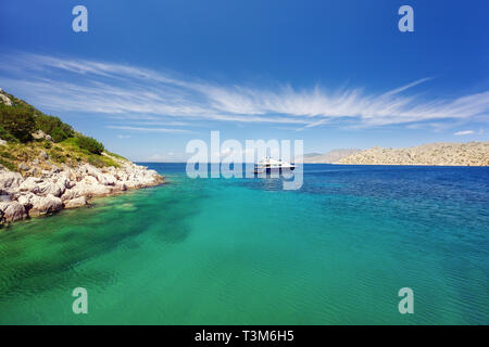 Das kristallklare türkisfarbene Wasser in einer Lagune in der Nähe von Bisti Strand auf der Insel Hydra in Griechenland. Nicht erkennbare Personen entspannen auf einer Luxusyacht mit Liegeplatz Seile Stockfoto