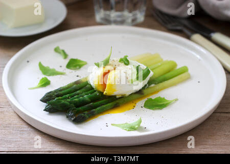 Frühstück mit pochiertem Ei und gekochten Spargel mit Butter und Salat auf einem hölzernen Oberfläche. Im rustikalen Stil. Stockfoto