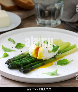 Frühstück mit pochiertem Ei und gekochten Spargel mit Butter und Salat auf einem hölzernen Oberfläche. Im rustikalen Stil. Stockfoto