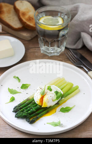 Frühstück mit pochiertem Ei und gekochten Spargel mit Butter und Salat auf einem hölzernen Oberfläche. Im rustikalen Stil. Stockfoto