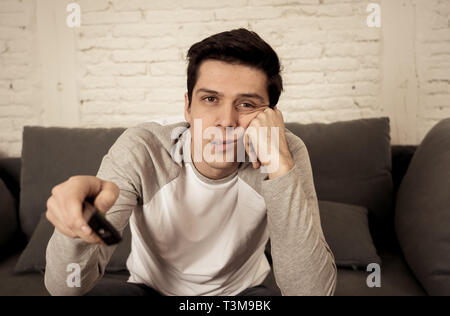 Lifestyle Portrait der junge Mann gelangweilt auf der Couch mit Fernbedienung zapping für Film oder Sport live. Suchen desinteressiert Bier trinkt. Bewegungsmangel und Stockfoto