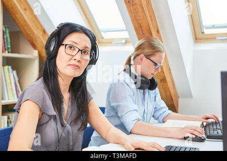 Junge asiatische Frau mit Headset bei e-learning Sprachkurs in der Volkshochschule Stockfoto