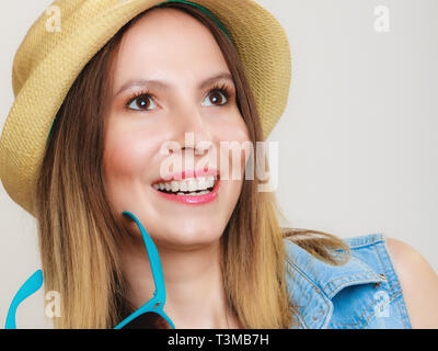 Urlaub. Glückliches Mädchen in Sommerkleidung blaue Sonnenbrille und Strohhut. Porträt von lächelnden Frau Tourist auf grau. Stockfoto