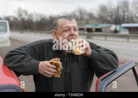 Portrait der Kaukasischen älterer Treiber gobbling lyulya Kebab in lavash in der Nähe von seinem Auto Stockfoto