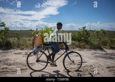 Ein Junge fährt mit dem Fahrrad in den Sand mit einem Sack von Nahrungsmittelhilfe für seine Familie in der Folge der massiven Cyclone Idai April 6, 2019 in Nhagau, Mosambik. Das World Food Programm, mit Hilfe von der US Air Force ist Transport der Hilfsgüter der verwüsteten Region zu unterstützen. Stockfoto