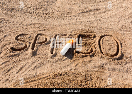 Sun Schutz Faktor 50. SPF 50 Wort auf dem Sand und weiße Flasche mit Sonnencreme geschrieben. Hautpflege Hintergrund. Stockfoto