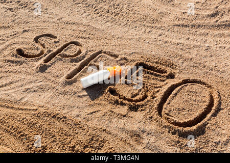 Sun Schutz Faktor 50. SPF 50 Wort auf dem Sand und weiße Flasche mit Sonnencreme geschrieben. Hautpflege Hintergrund. Stockfoto