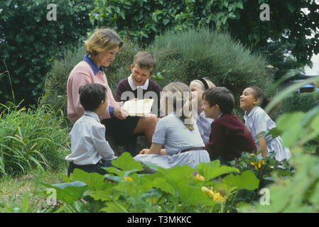 Eine kleine Klasse der Kinder hören eine Geschichte lesen, die von Ihrem Lehrer. England, Großbritannien Stockfoto