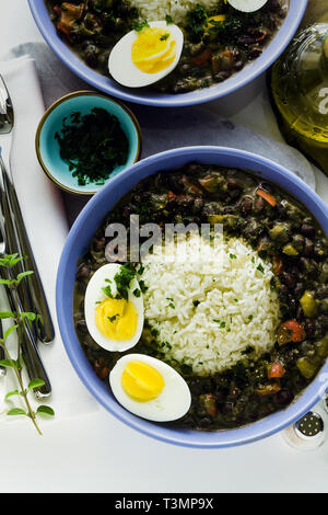 Reis mit schwarzen Bohnen und gekochtes Ei auf den Tisch mit Gewürzen und Olivenöl. Gesunde karibisches Essen Stockfoto