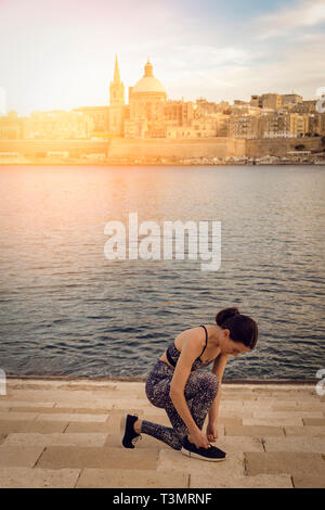 Frau, die ihre Laufschuhe mit Valletta Stadt Hintergrund mit Sun lens flare Stockfoto