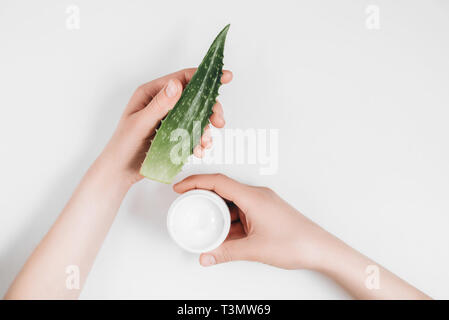 7/8-Ansicht von weiblichen Händen mit organischen Creme und Aloe Vera Blatt auf weißem Hintergrund. Flach, oben Anzeigen, Kopieren, minimalistisch eingerichtet. Schönheit Konzept. Stockfoto