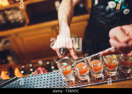 Barkeeper gießen stark alkoholisches Getränk in kleinen Gläsern auf Bar, Schüsse Stockfoto