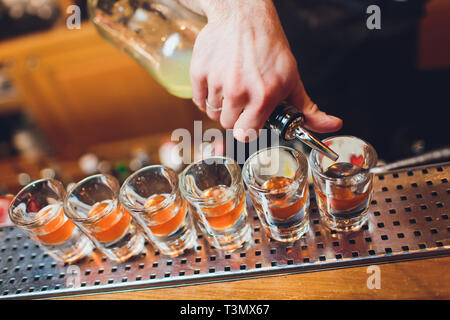 Barkeeper gießen stark alkoholisches Getränk in kleinen Gläsern auf Bar, Schüsse Stockfoto