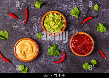 Mexikanisches Essen Hintergrund: Guacamole, Salsa, cheesy Saucen mit Zutaten auf schwarzem Hintergrund, Ansicht von oben. Stockfoto