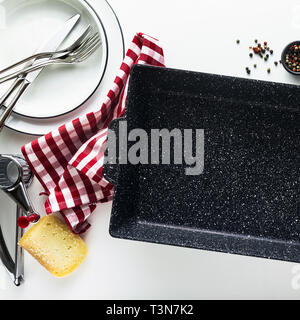 Leere schwarze Keramik Lasagne Auflaufform auf einem weißen Tisch mit Gewürzen und Pflanzenöl. Hintergrund Kochen im Ofen Stockfoto