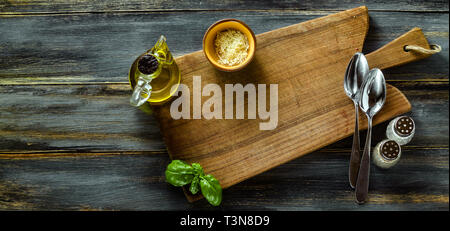 Banner der Schneiden Brett aus Olivenholz auf einem blauen Holztisch mit Olivenöl, Basilikum und Parmesan. Mediterrane Tabelle einstellen Stockfoto