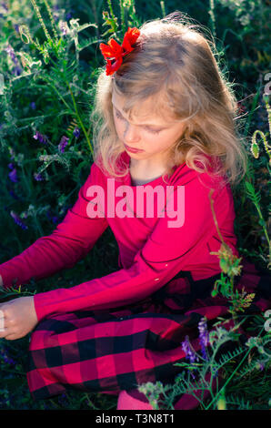 Schöne blonde Mädchen in Blumen und Gras sitzen Stockfoto
