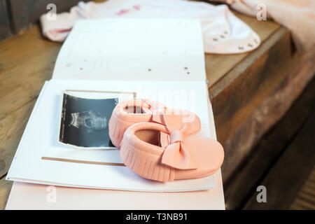 Baby girl rosa Kleid Kleidung mit Neugeborenen Buch album, Körper und kleine Schuhe und Ultraschalluntersuchung fetale Foto auf Fenster Holz Fensterbank Hintergrund. Stockfoto