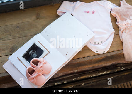 Baby girl rosa Kleid Kleidung mit Neugeborenen Buch album, Körper und kleine Schuhe und Ultraschalluntersuchung fetale Foto auf Fenster Holz Fensterbank Hintergrund. Stockfoto