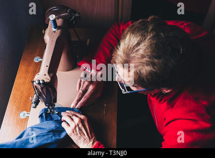 Nahaufnahme der älteren Frau Näherin Hände nähen Bekleidung Detail auf manuelle Nähmaschine. Handgemachte exklusive Kleidung und Reparatur, private Busi Stockfoto