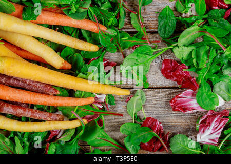 Frische organische rainbow Karotten auf frischem Salat auf Holz- Hintergrund. Stockfoto