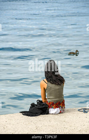 Gardasee, Italien - September 2018: Junge Person sitzen auf den Rand des Gardasees mit Blick über das ruhige Wasser. Stockfoto