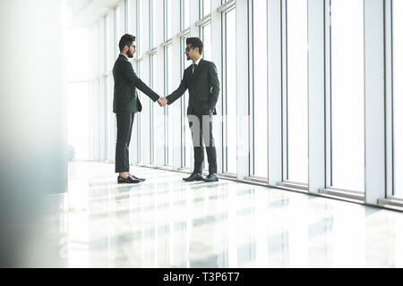 Zwei indische Unternehmer die Hände schütteln bei grossen Fenster mit urbanen Stadtlandschaft, zuversichtlich Geschäftspartner handshaking im Amt. Seitenansicht Stockfoto