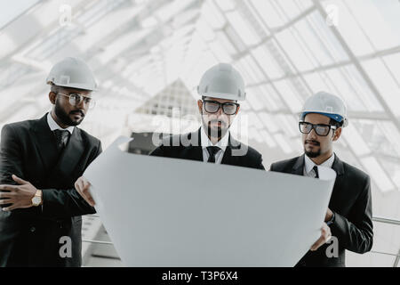 Nahaufnahme von drei indischen Geschäftsleuten Helme tragen und an neue, moderne Gebäude Hintergrund. Architekten Konzept. Stockfoto