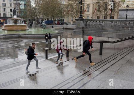 Jugendliche springen Sie die Schritte, die Regen auf dem Trafalgar Square, Westminster, zu entkommen, am 9. April 2019 in London, England. Stockfoto