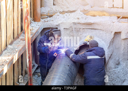 Schweißer Schweißen Wasser oder Gas stahl Pipeline mit Assistant Arbeiter in einen Graben. Stadt u-Utilitys Erneuerung und replacemen Stockfoto