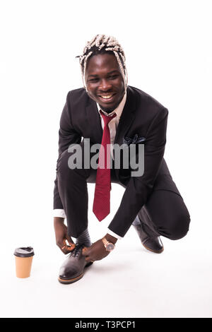 Crouching afrikanischen Geschäftsmann Schnürsenkel binden an Kamera schaut. Voller Körper Länge Porträt über weiße studio Hintergrund isoliert. Stockfoto