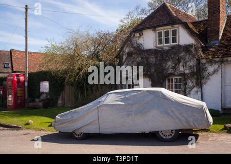 Ein großer Klassiker mit einem grauen Car Cover und eine rote Telefonzelle im Turville Dorfzentrum Stockfoto