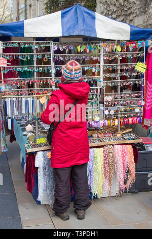 Ein Markt Standbesitzer in einem hellen roten Mantel und Tibetischen Hut in Oxford eingeführte Schmuck Stockfoto