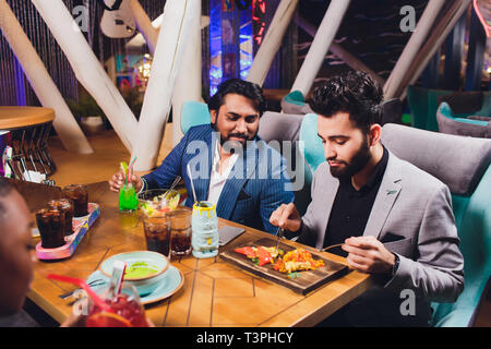 Zwei Mann in Bar halten Gläser Sitzen an der Theke, Trinken Cocktail, fröhliche Freunde treffen Bar zu sprechen. Stockfoto
