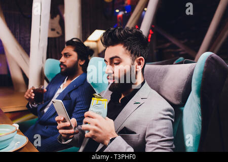 Zwei Mann in Bar halten Gläser Sitzen an der Theke, Trinken Cocktail, fröhliche Freunde treffen Bar zu sprechen. Stockfoto