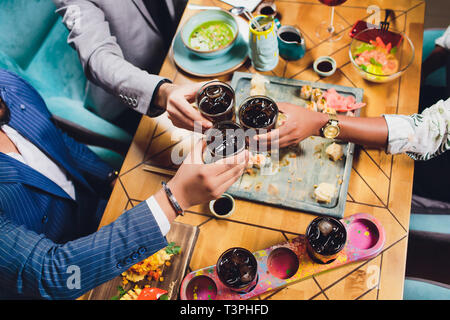 Hände von Freunden, die zusammen im Kreis mit den verschiedenen Cocktails mit Eis auf dem Hintergrund der alten Holztisch Oberfläche. Ansicht von oben. Stockfoto