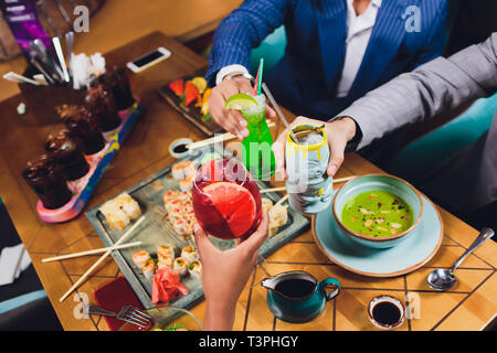 Hände von Freunden, die zusammen im Kreis mit den verschiedenen Cocktails mit Eis auf dem Hintergrund der alten Holztisch Oberfläche. Ansicht von oben. Stockfoto