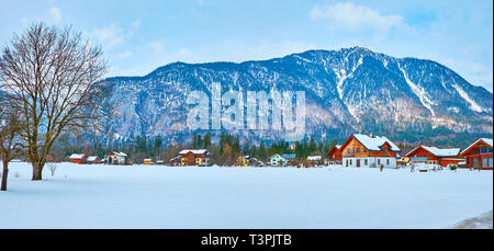 Panorama von Obertraun mit zahlreichen Holzhütten und großen verschneite Feld im Vordergrund, Salzkammergut, Österreich. Stockfoto